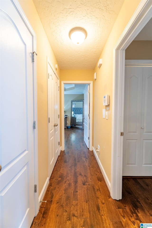 corridor featuring dark wood-style floors, a textured ceiling, and baseboards