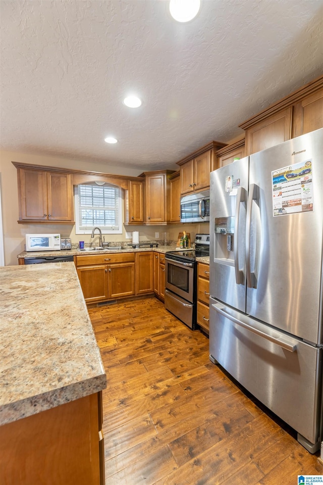 kitchen featuring brown cabinets, dark wood finished floors, light countertops, appliances with stainless steel finishes, and a sink