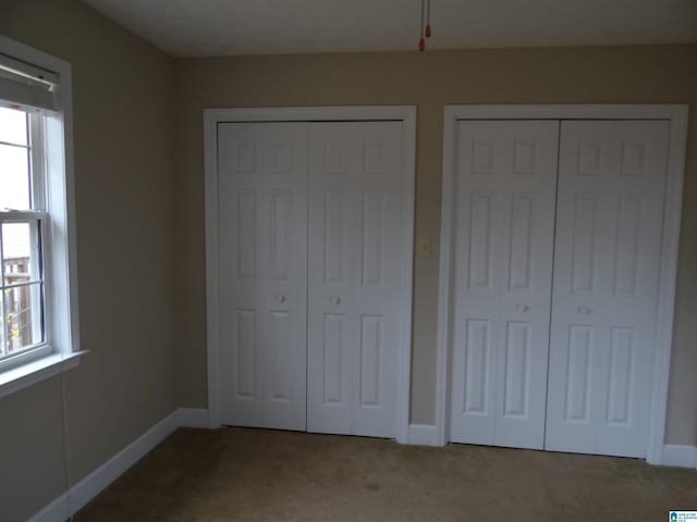 unfurnished bedroom featuring baseboards, multiple windows, carpet, and multiple closets