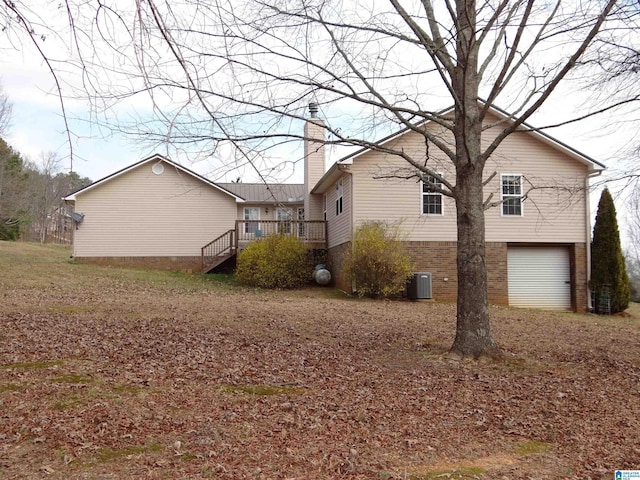 view of side of home featuring brick siding, a chimney, central air condition unit, a deck, and a garage