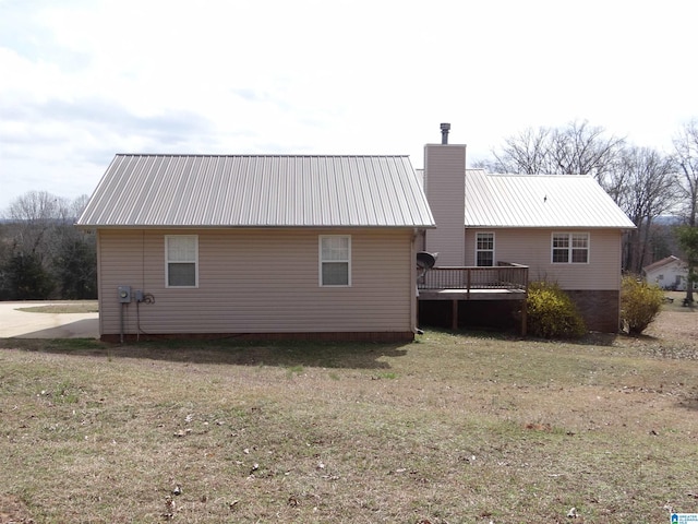 rear view of house featuring a deck, metal roof, a chimney, and a lawn