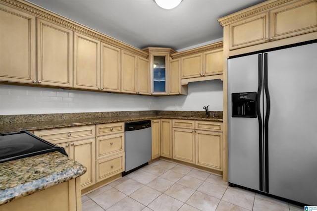 kitchen with light tile patterned floors, stainless steel appliances, dark stone counters, and a sink