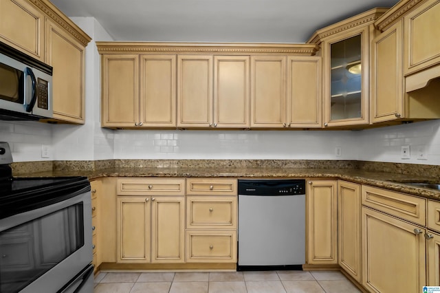 kitchen with stainless steel appliances, dark stone counters, light tile patterned flooring, and glass insert cabinets