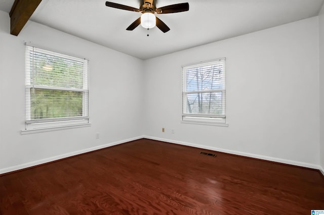 empty room with dark wood-style flooring, visible vents, and baseboards