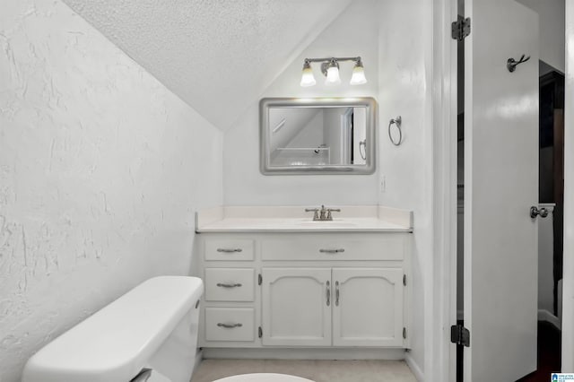 bathroom featuring a textured ceiling, a textured wall, toilet, vanity, and vaulted ceiling