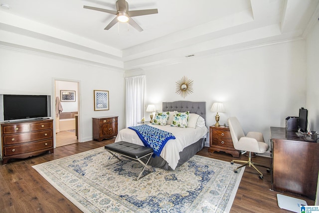 bedroom with dark wood-style floors, a ceiling fan, a raised ceiling, and connected bathroom