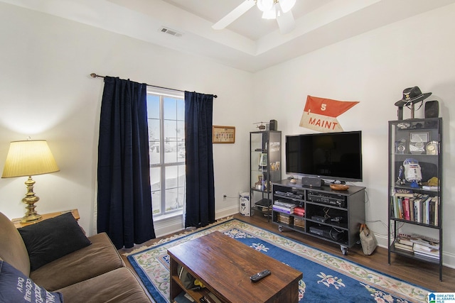 living room with ceiling fan, wood finished floors, visible vents, baseboards, and a tray ceiling