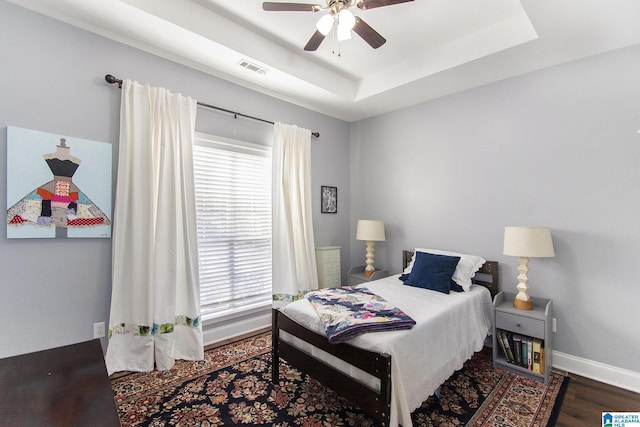 bedroom featuring wood finished floors, a raised ceiling, a ceiling fan, and baseboards