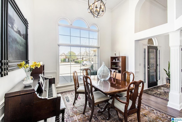 dining room with crown molding, a towering ceiling, an inviting chandelier, wood finished floors, and ornate columns