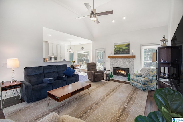 living room featuring high vaulted ceiling, a healthy amount of sunlight, a stone fireplace, and wood finished floors