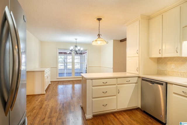 kitchen featuring wood finished floors, a peninsula, stainless steel appliances, light countertops, and backsplash