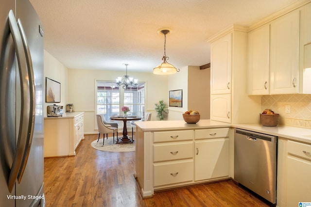 kitchen with a peninsula, wood finished floors, light countertops, appliances with stainless steel finishes, and decorative backsplash