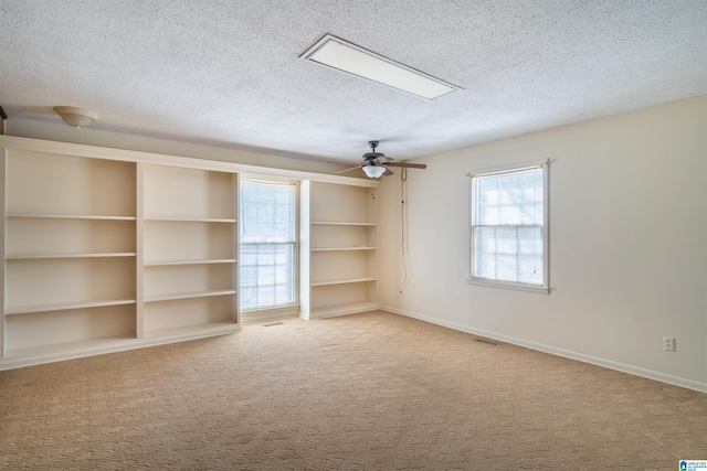 carpeted empty room featuring a textured ceiling, ceiling fan, visible vents, and baseboards