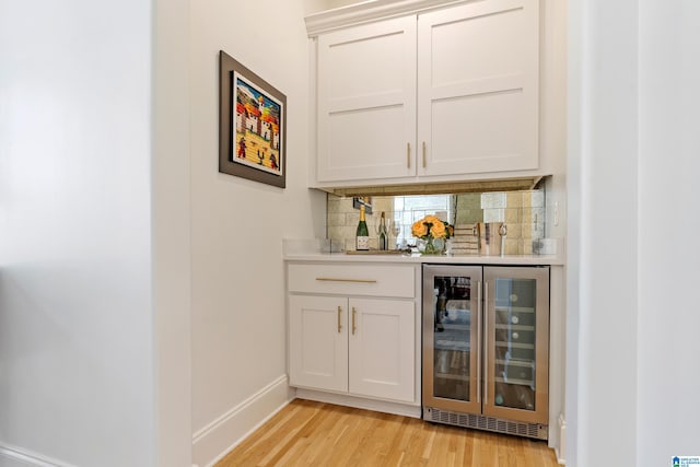 bar featuring light wood finished floors, tasteful backsplash, baseboards, wine cooler, and a dry bar