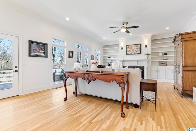 living area with built in shelves, light wood-style flooring, a fireplace, crown molding, and baseboards