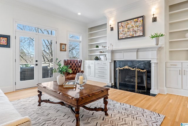 living area with built in features, light wood-type flooring, a fireplace, and crown molding