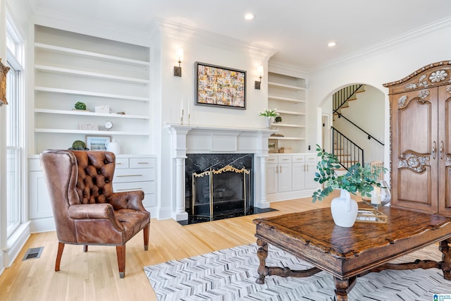 living area featuring visible vents, light wood-style flooring, built in features, a high end fireplace, and crown molding