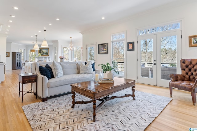 living area featuring french doors, light wood-style floors, a healthy amount of sunlight, and crown molding