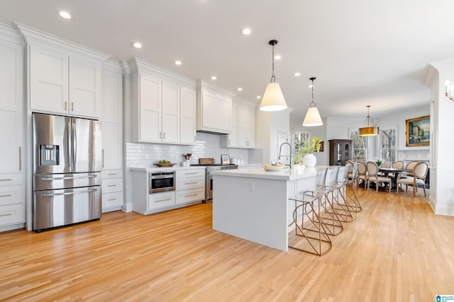 kitchen featuring a breakfast bar, light wood-style flooring, light countertops, appliances with stainless steel finishes, and backsplash