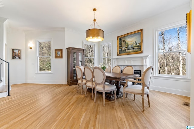 dining area with a high end fireplace, light wood-style flooring, stairs, and ornamental molding