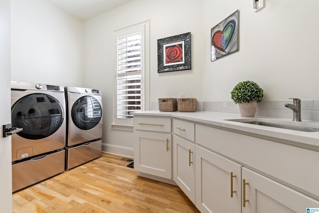 washroom with baseboards, light wood finished floors, cabinet space, a sink, and independent washer and dryer