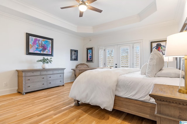 bedroom featuring a tray ceiling, light wood-style flooring, ornamental molding, and french doors