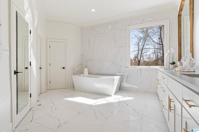 full bathroom with marble finish floor, stone wall, a freestanding bath, and crown molding