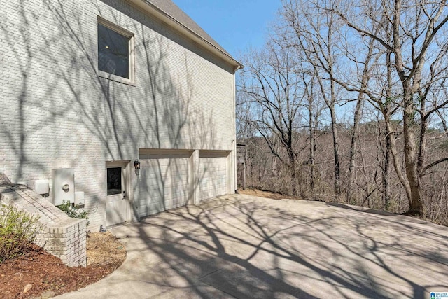 view of side of property featuring a garage, brick siding, and concrete driveway