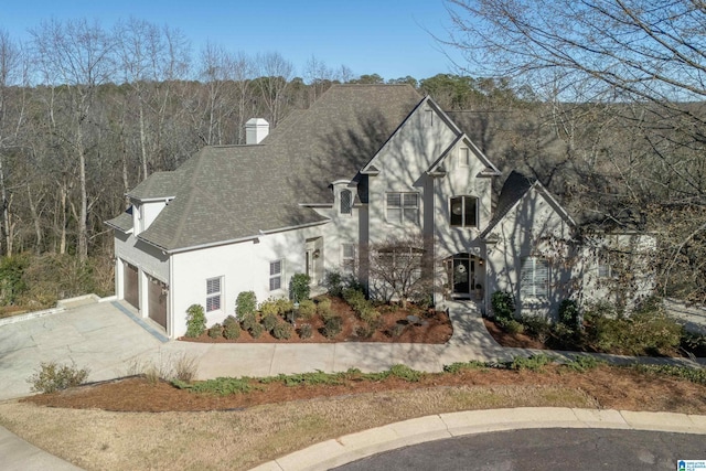 view of front of home with a forest view, a shingled roof, stucco siding, a garage, and driveway