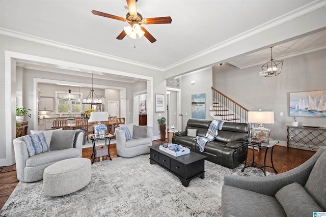 living area with stairway, ornamental molding, ceiling fan with notable chandelier, and wood finished floors