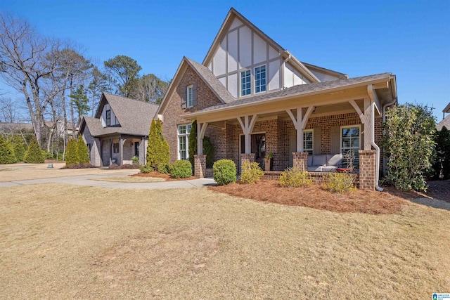 tudor-style house featuring a porch, brick siding, and a front lawn