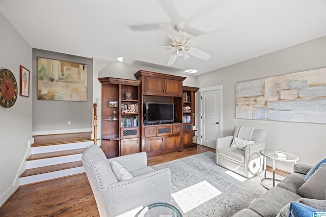 living room featuring stairs, baseboards, dark wood-style floors, and a ceiling fan