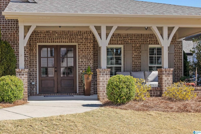 property entrance with brick siding, covered porch, french doors, and a shingled roof