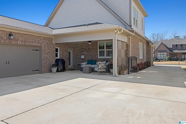 view of property exterior featuring brick siding, concrete driveway, outdoor lounge area, a ceiling fan, and a patio