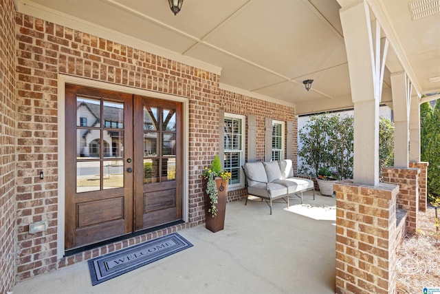 property entrance featuring visible vents, covered porch, french doors, and brick siding