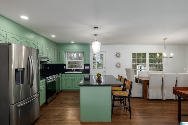 kitchen with a sink, under cabinet range hood, appliances with stainless steel finishes, green cabinets, and dark countertops