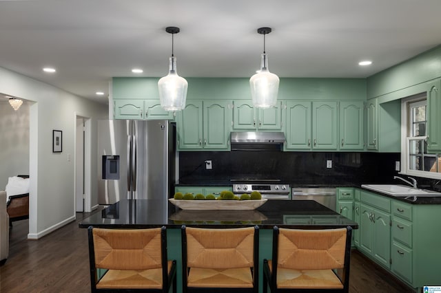 kitchen with dark countertops, a sink, under cabinet range hood, appliances with stainless steel finishes, and green cabinetry