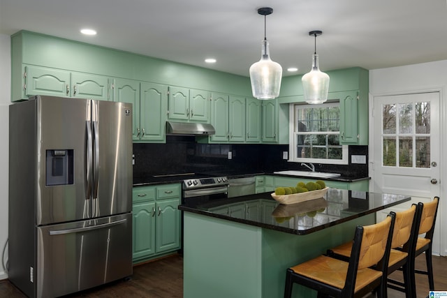 kitchen with under cabinet range hood, a sink, dark countertops, stainless steel fridge, and dishwashing machine