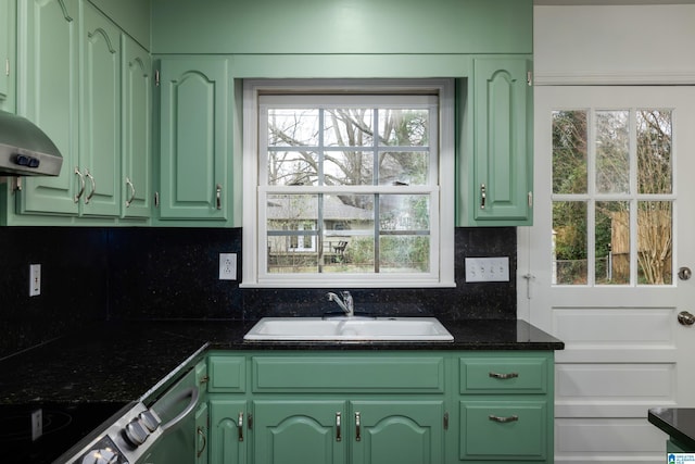 kitchen featuring dark countertops, backsplash, green cabinets, and a sink