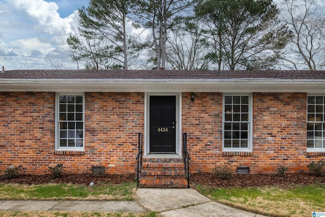 property entrance featuring crawl space, brick siding, and a shingled roof