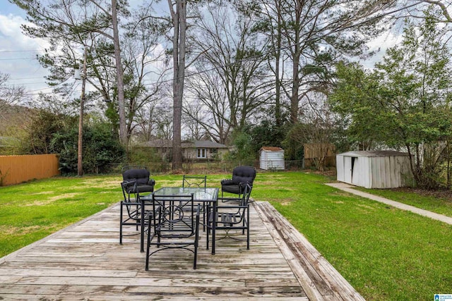 wooden terrace featuring outdoor dining space, a fenced backyard, an outdoor structure, a storage unit, and a lawn