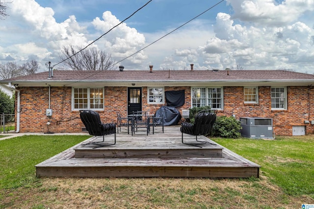 rear view of property with a lawn, a deck, roof with shingles, brick siding, and central AC unit