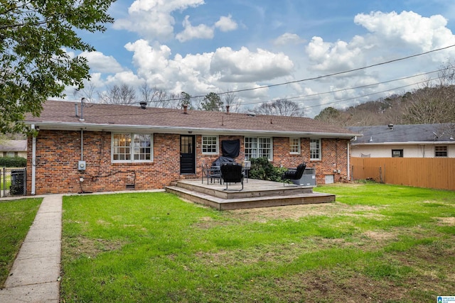 back of house featuring brick siding, a lawn, and fence