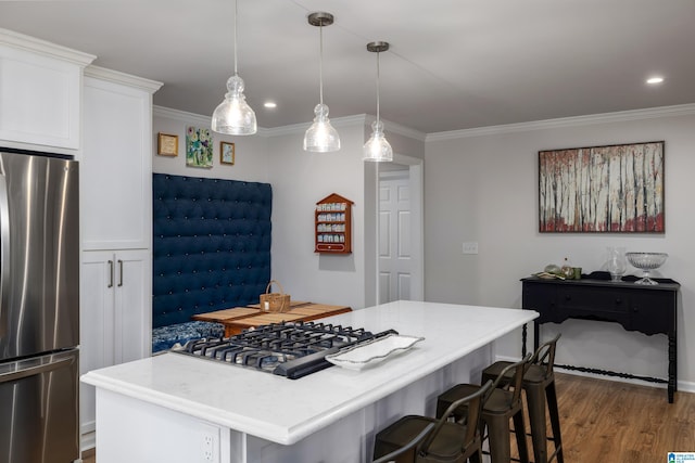 kitchen featuring wood finished floors, a kitchen island, ornamental molding, stainless steel appliances, and white cabinets