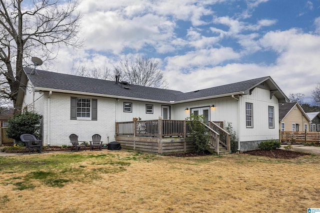 back of house featuring brick siding, a wooden deck, roof with shingles, a lawn, and french doors