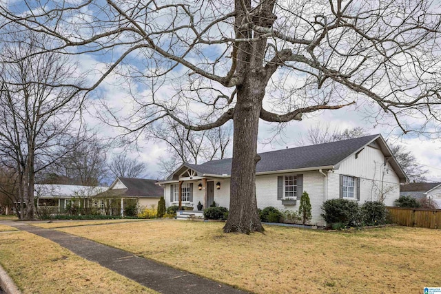 view of front of property with a front yard, fence, brick siding, and a shingled roof