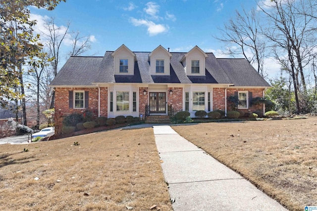 new england style home featuring brick siding, roof with shingles, and a front lawn