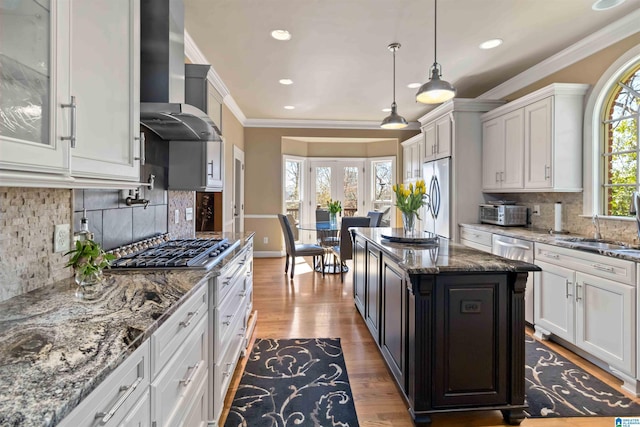 kitchen featuring ornamental molding, dark stone countertops, wood finished floors, stainless steel appliances, and wall chimney exhaust hood