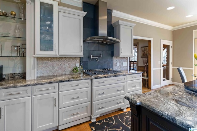 kitchen with glass insert cabinets, wall chimney exhaust hood, crown molding, and stainless steel gas cooktop