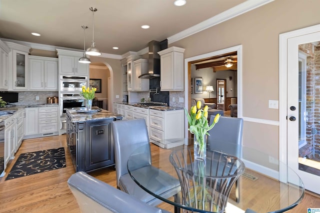 kitchen with stainless steel appliances, arched walkways, wall chimney exhaust hood, and white cabinetry